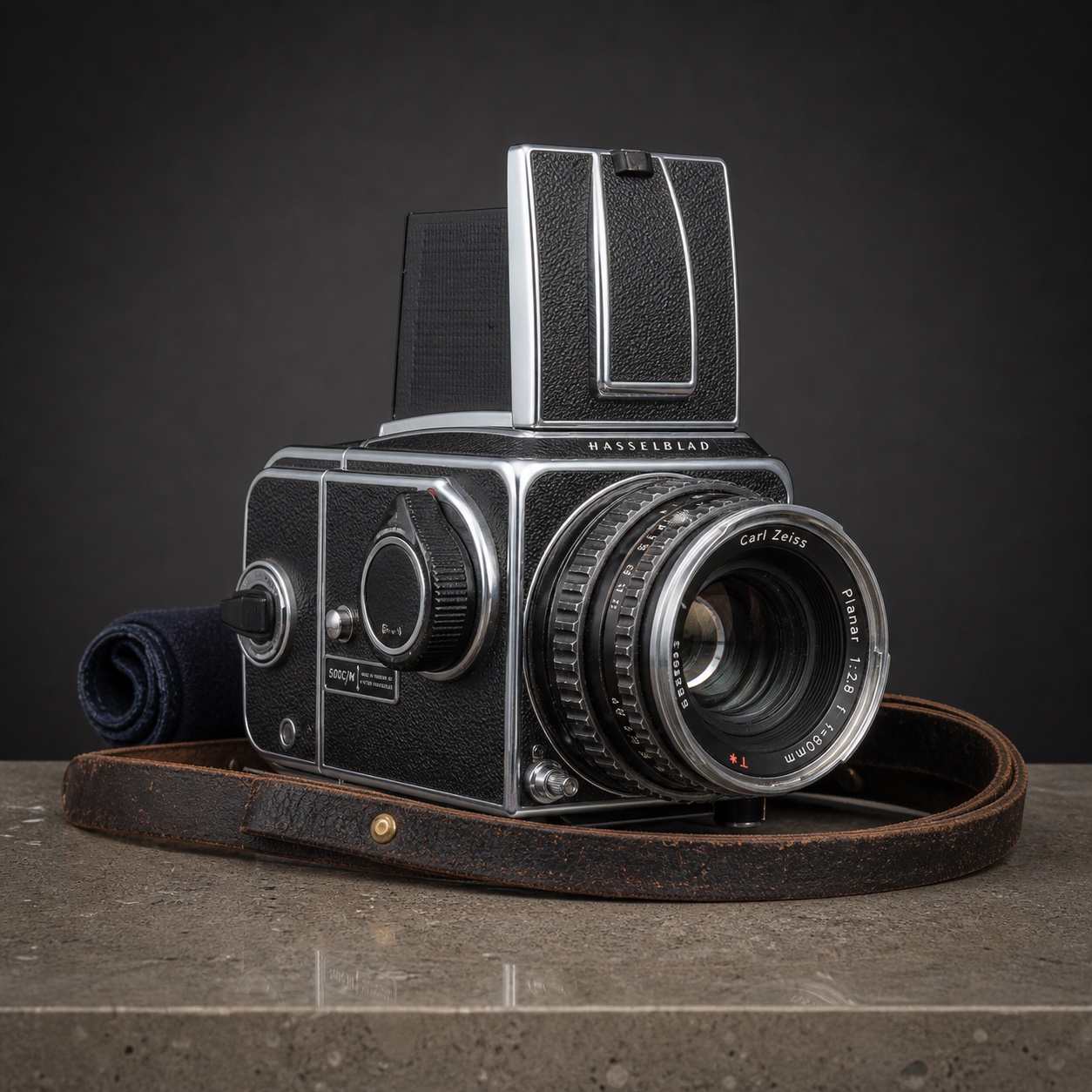 Vintage Hasselblad 500C/M medium-format camera on a polished concrete pedestal with leather strap coiled at the base